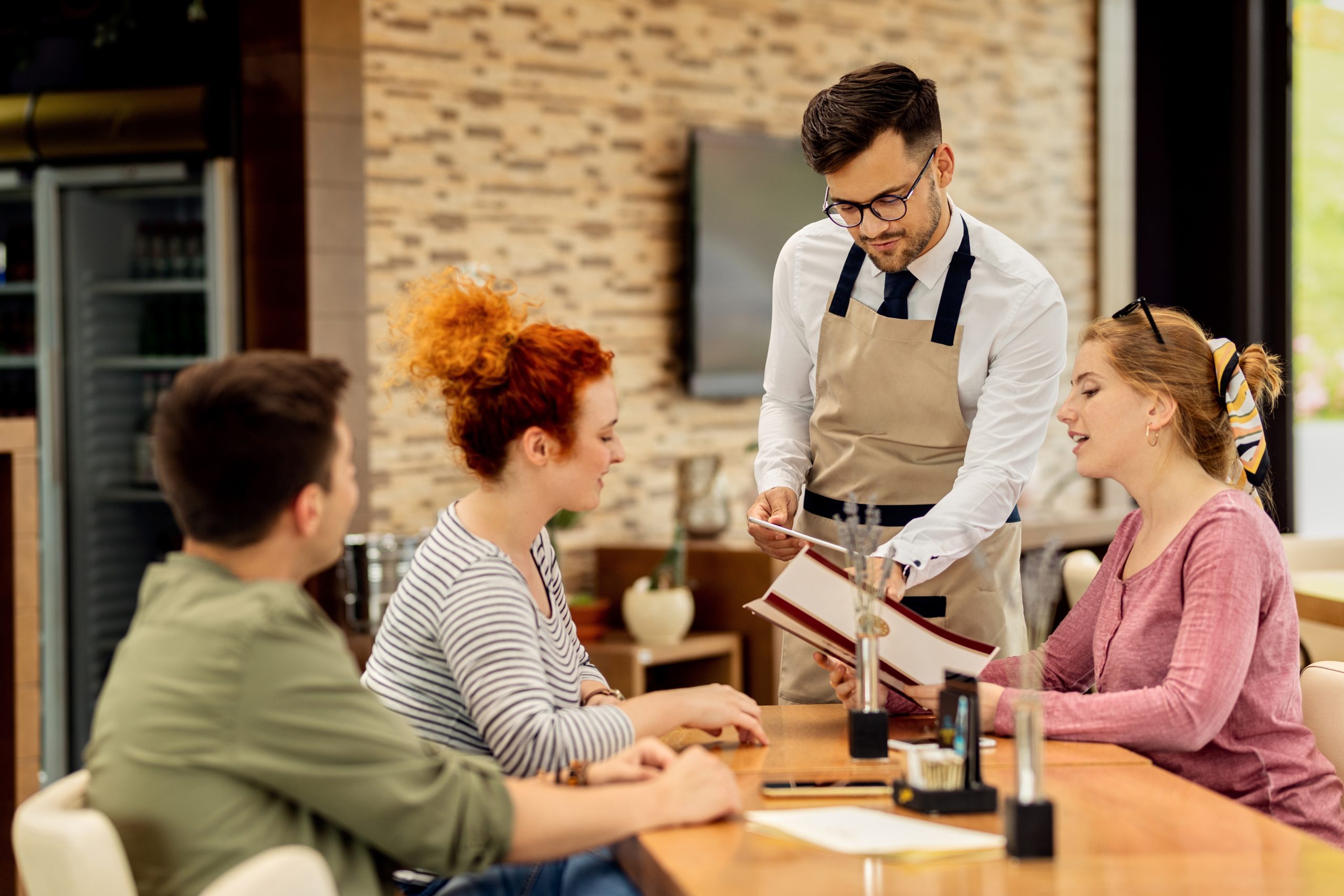 Young waiter recommending to guests what to order from the menu